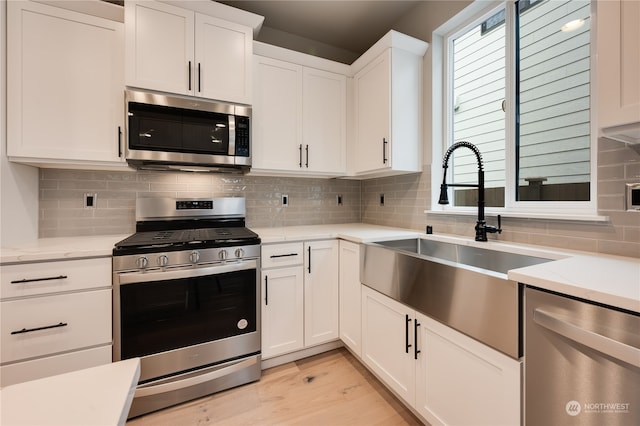 kitchen featuring appliances with stainless steel finishes, tasteful backsplash, white cabinetry, sink, and light hardwood / wood-style floors