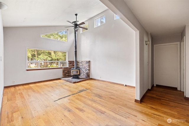 unfurnished living room featuring ceiling fan, high vaulted ceiling, light hardwood / wood-style flooring, and a wood stove