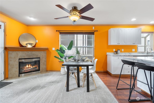 dining room featuring sink, a tiled fireplace, ornamental molding, ceiling fan, and light hardwood / wood-style flooring