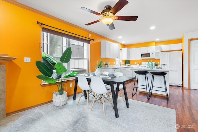 dining space with sink, dark wood-type flooring, ornamental molding, and ceiling fan