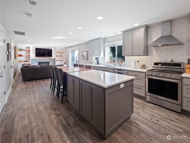 kitchen featuring wall chimney range hood, gray cabinets, stainless steel appliances, and a kitchen island