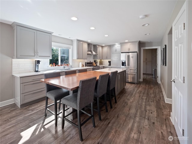 kitchen with wood counters, wall chimney exhaust hood, a breakfast bar area, tasteful backsplash, and high quality appliances