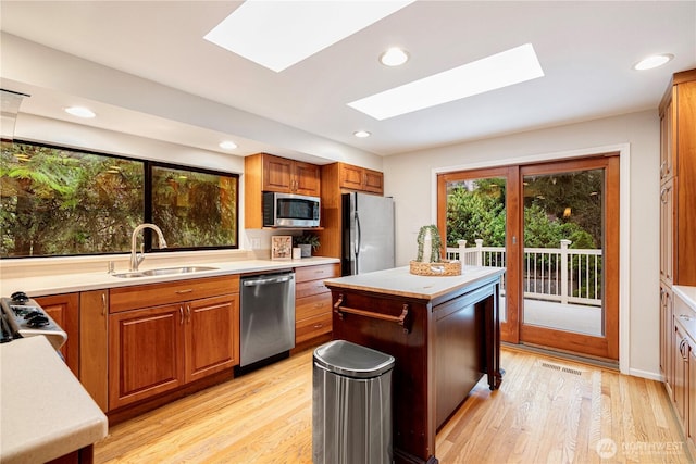 kitchen with appliances with stainless steel finishes, light countertops, a sink, and a skylight