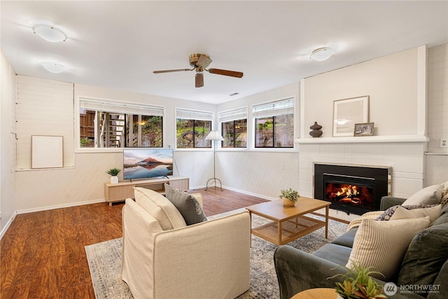 living area featuring a tile fireplace, baseboards, a ceiling fan, and wood finished floors