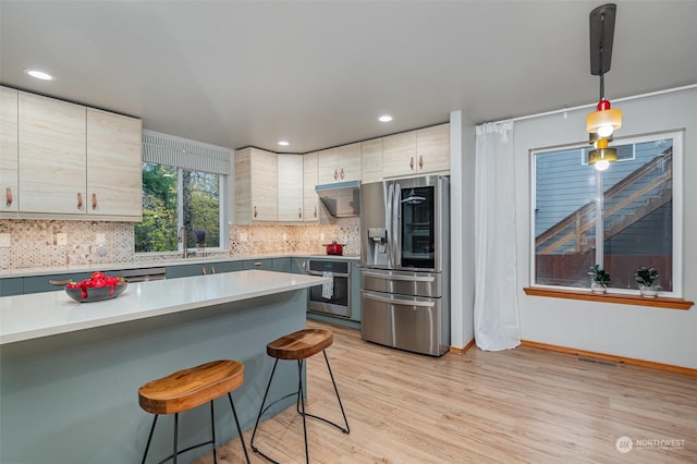 kitchen with a breakfast bar, tasteful backsplash, hanging light fixtures, appliances with stainless steel finishes, and light hardwood / wood-style floors