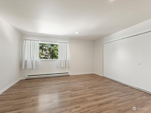 unfurnished bedroom featuring a baseboard radiator, a closet, and wood-type flooring