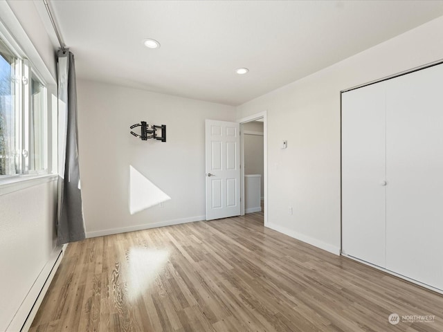 unfurnished bedroom with baseboard heating, light hardwood / wood-style floors, and a closet