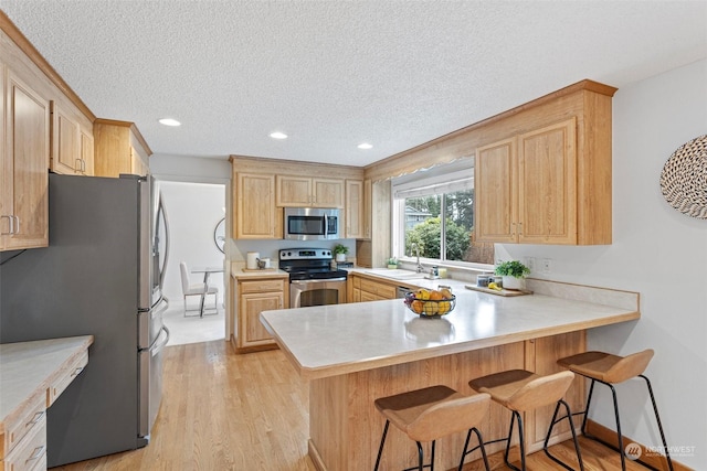 kitchen with appliances with stainless steel finishes, light brown cabinetry, a kitchen breakfast bar, and kitchen peninsula