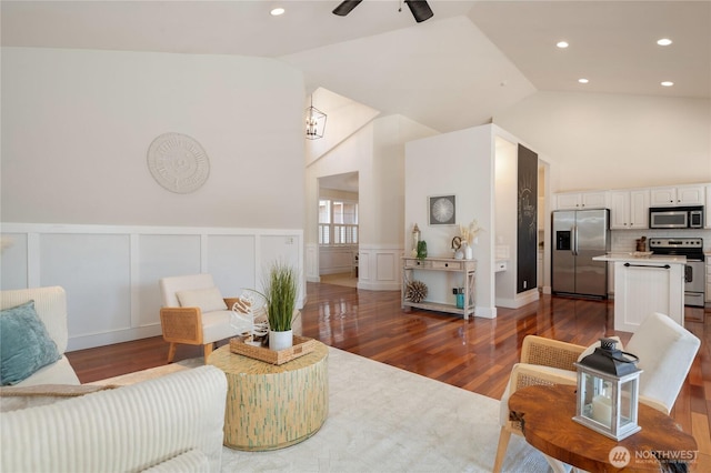 living room featuring dark wood-style floors, high vaulted ceiling, wainscoting, and a decorative wall