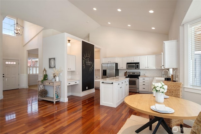 kitchen featuring appliances with stainless steel finishes, dark wood-type flooring, white cabinetry, a kitchen island, and high vaulted ceiling