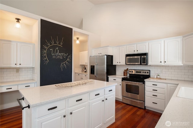 kitchen featuring light stone counters, stainless steel appliances, white cabinets, a center island, and dark wood finished floors