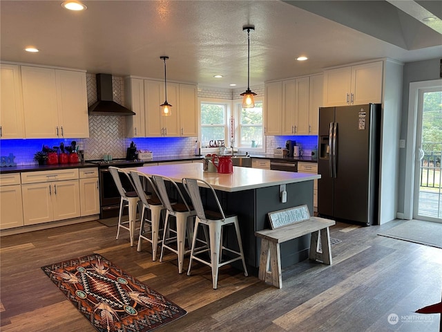 kitchen featuring white cabinetry, a center island, hanging light fixtures, wall chimney range hood, and black appliances