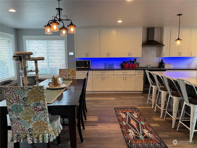 kitchen with stainless steel appliances, decorative light fixtures, white cabinets, and wall chimney exhaust hood