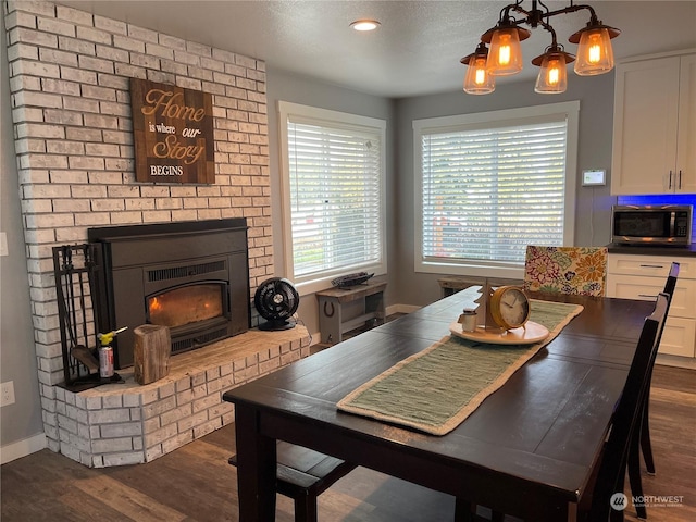 dining room featuring a brick fireplace, a chandelier, a textured ceiling, and dark hardwood / wood-style flooring