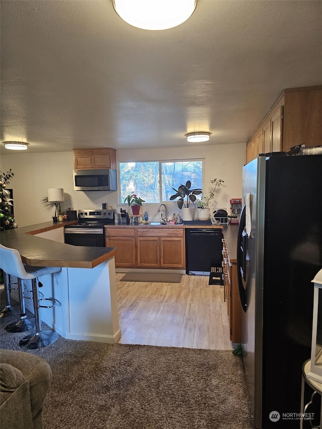 kitchen with a textured ceiling, stainless steel appliances, a kitchen breakfast bar, and kitchen peninsula