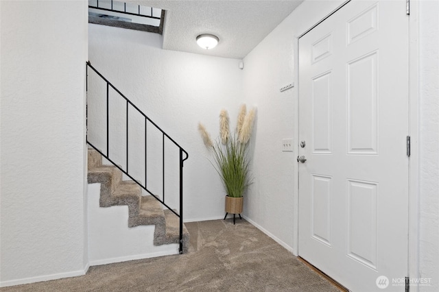 carpeted foyer with a textured ceiling, baseboards, and stairs