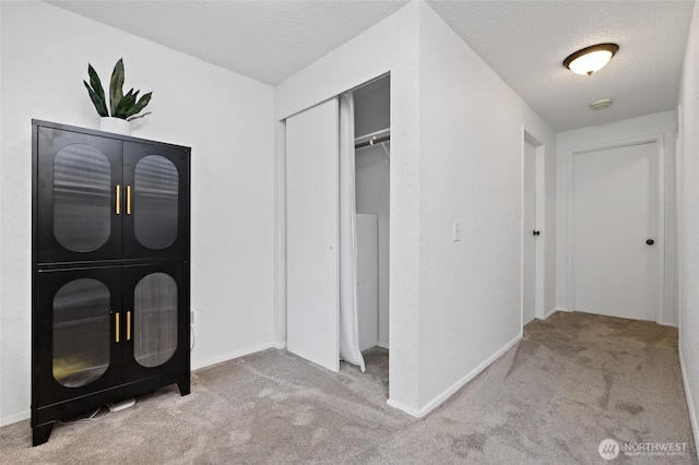 interior space with a closet, light colored carpet, a textured ceiling, and baseboards