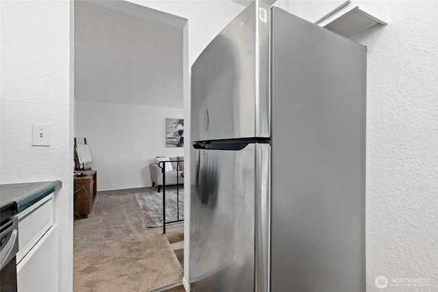 kitchen featuring a textured wall, carpet, and freestanding refrigerator