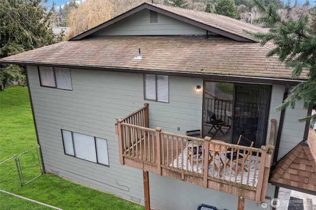 back of house featuring a shingled roof and a lawn