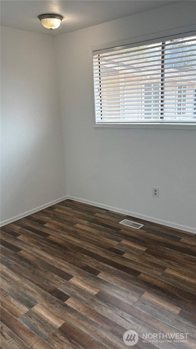 spare room featuring dark wood-style floors, visible vents, and baseboards