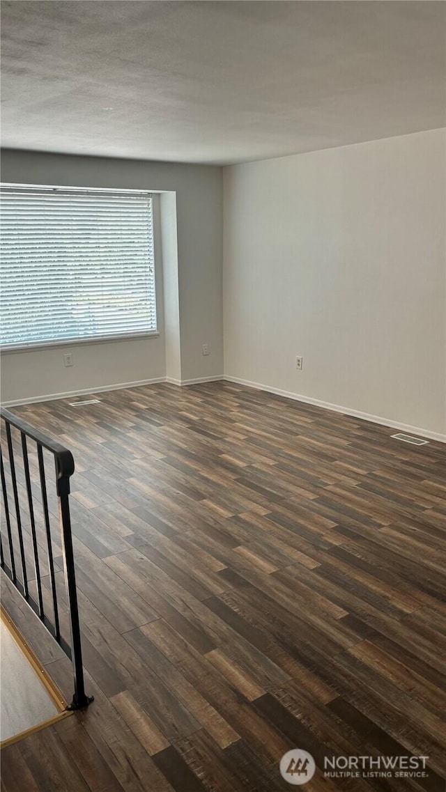 spare room with baseboards and dark wood-type flooring