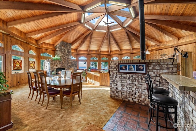 dining room featuring wood ceiling, a stone fireplace, vaulted ceiling with skylight, and wood walls