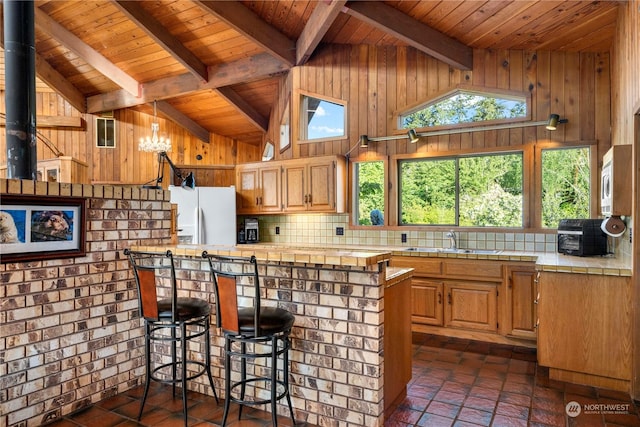 kitchen featuring sink, white fridge with ice dispenser, tile countertops, kitchen peninsula, and wood walls