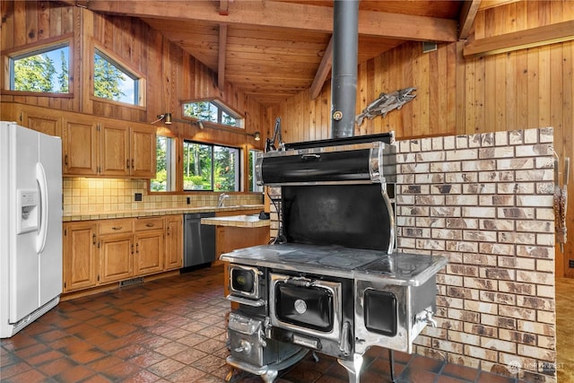 kitchen featuring dishwasher, wood walls, tasteful backsplash, white fridge with ice dispenser, and a wood stove