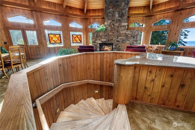 staircase featuring beam ceiling, a stone fireplace, wood walls, and carpet flooring