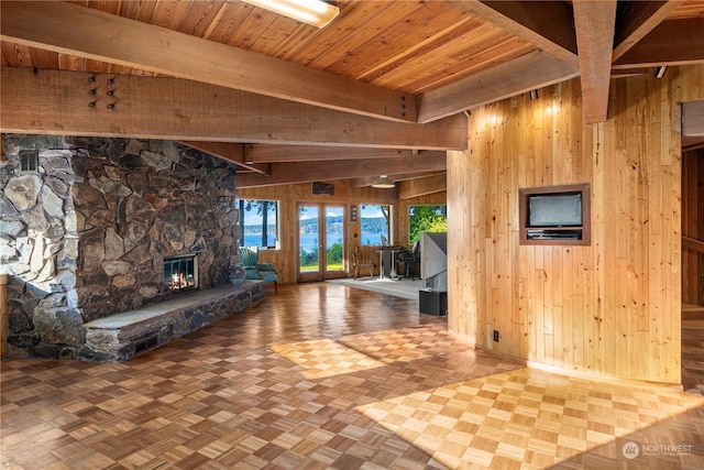 unfurnished living room featuring beam ceiling, a stone fireplace, and wooden walls