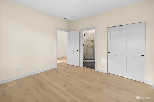 unfurnished bedroom featuring a closet, light wood-type flooring, and ensuite bath