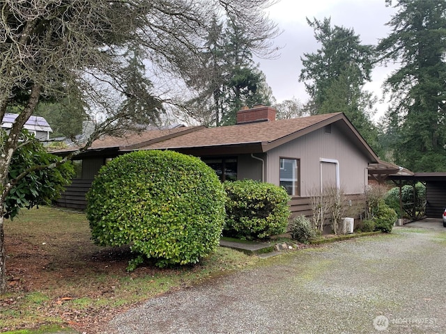 view of side of property with a carport, a shingled roof, and a chimney