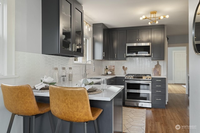 kitchen with a breakfast bar area, appliances with stainless steel finishes, dark hardwood / wood-style flooring, decorative backsplash, and kitchen peninsula