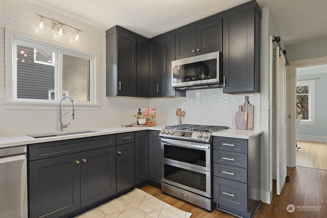 kitchen with sink, light hardwood / wood-style flooring, backsplash, stainless steel appliances, and a barn door