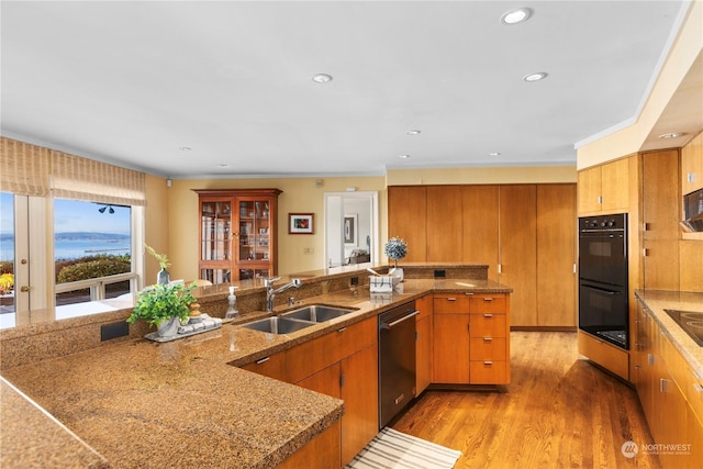 kitchen with hardwood / wood-style floors, sink, dishwashing machine, black double oven, and kitchen peninsula