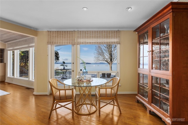 dining space with crown molding, a water view, and light hardwood / wood-style flooring