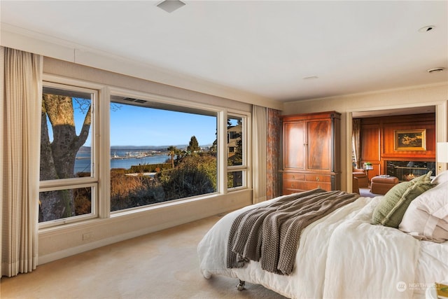 bedroom featuring ornamental molding, a water view, light colored carpet, and a fireplace