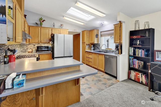 kitchen featuring lofted ceiling with skylight, sink, decorative backsplash, kitchen peninsula, and stainless steel appliances