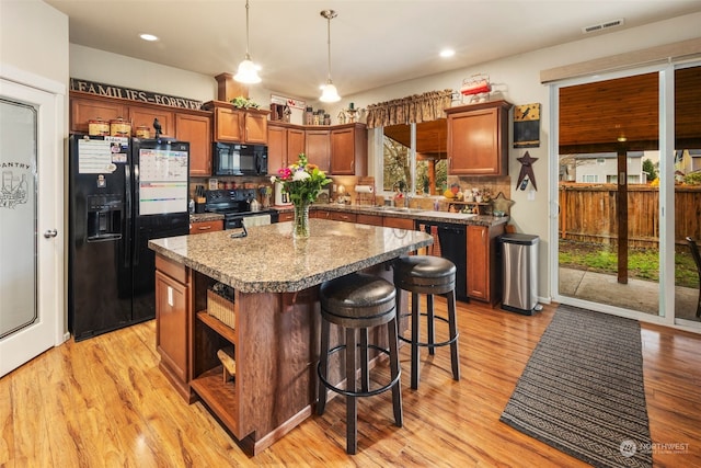 kitchen with a kitchen island, light hardwood / wood-style flooring, pendant lighting, and black appliances