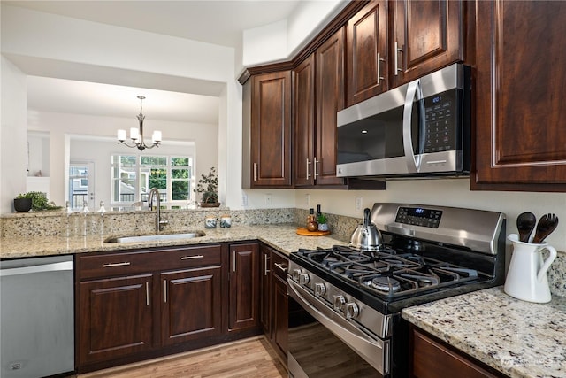 kitchen with dark brown cabinetry, sink, decorative light fixtures, stainless steel appliances, and light stone countertops