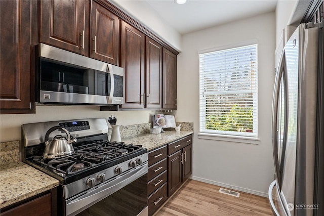 kitchen featuring dark brown cabinetry, light stone countertops, appliances with stainless steel finishes, and light wood-type flooring