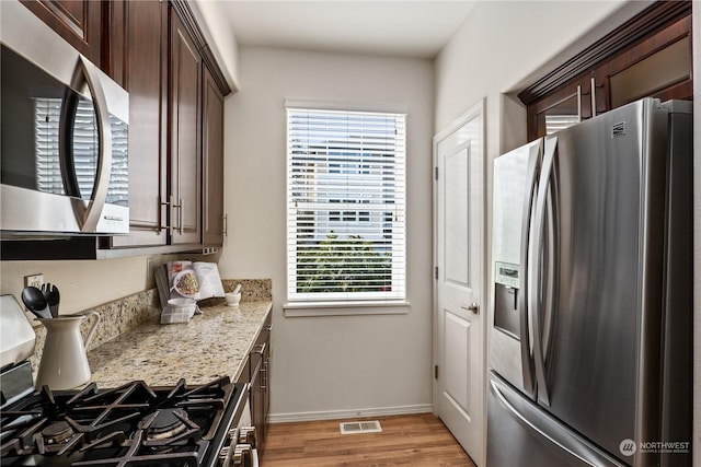 kitchen with stainless steel appliances, light stone countertops, dark brown cabinets, and light wood-type flooring