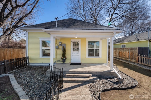 shotgun-style home with a shingled roof, fence private yard, and covered porch