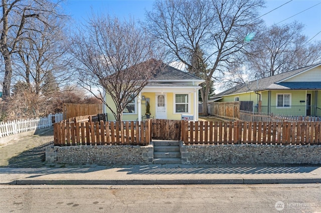 view of front of home featuring a porch, a fenced front yard, and a shingled roof