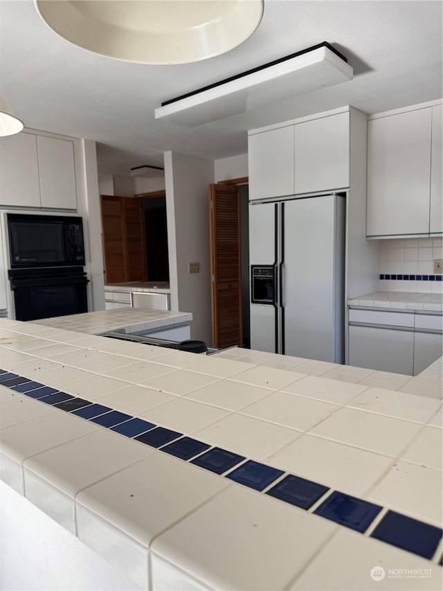 kitchen featuring tasteful backsplash, white cabinets, tile countertops, and black appliances