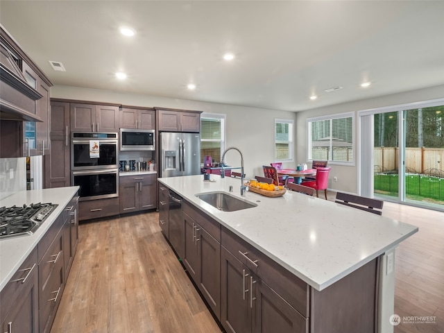 kitchen with a kitchen island with sink, sink, light stone counters, and appliances with stainless steel finishes