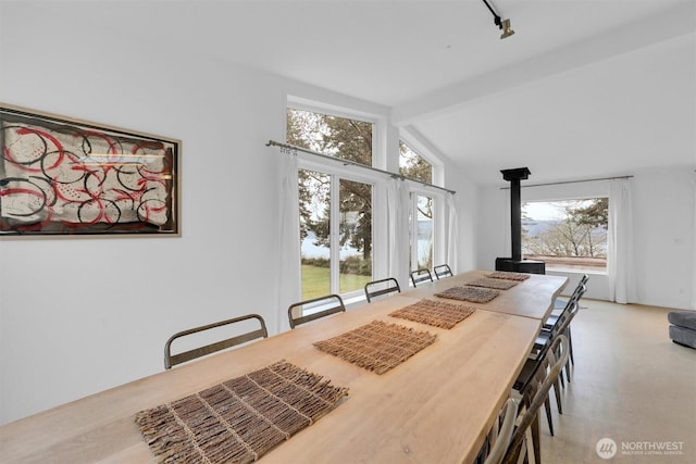 dining space with vaulted ceiling with beams, light carpet, and a wood stove