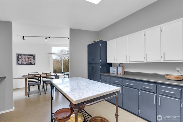 kitchen with blue cabinetry, light countertops, white cabinets, track lighting, and baseboards