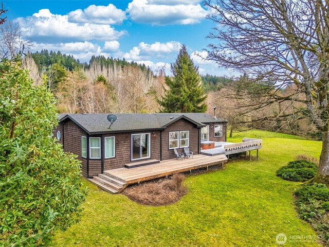 back of property with a wooden deck, a view of trees, and a yard