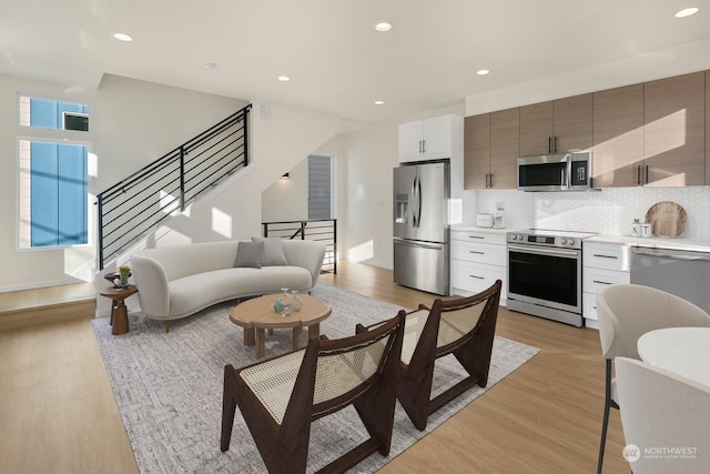 kitchen with tasteful backsplash, stainless steel appliances, white cabinets, and light wood-type flooring